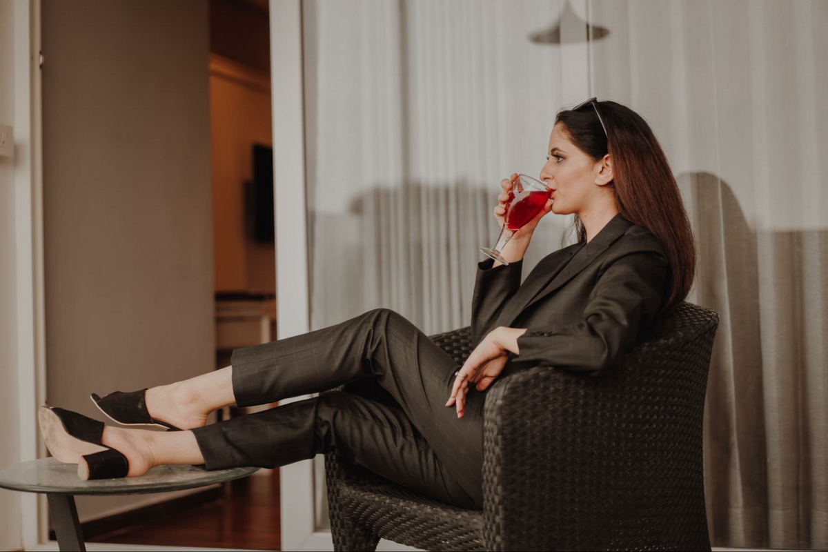 a woman in a grey suit drinking wine in a grey chair, as featured in The Wine Movers’ blog on professional wine movers and moving a wine collection